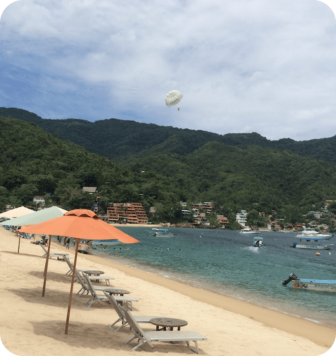 A peaceful beach with umbrellas, lounge chairs, and distant hills under a cloudy sky.